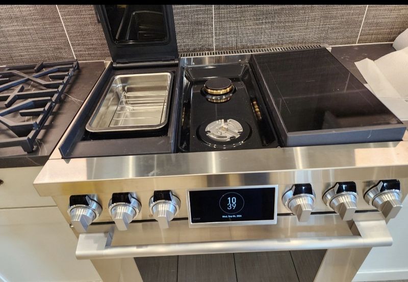 Modern stainless steel stovetop with multiple burners, knobs, control panel, and built-in compartments.