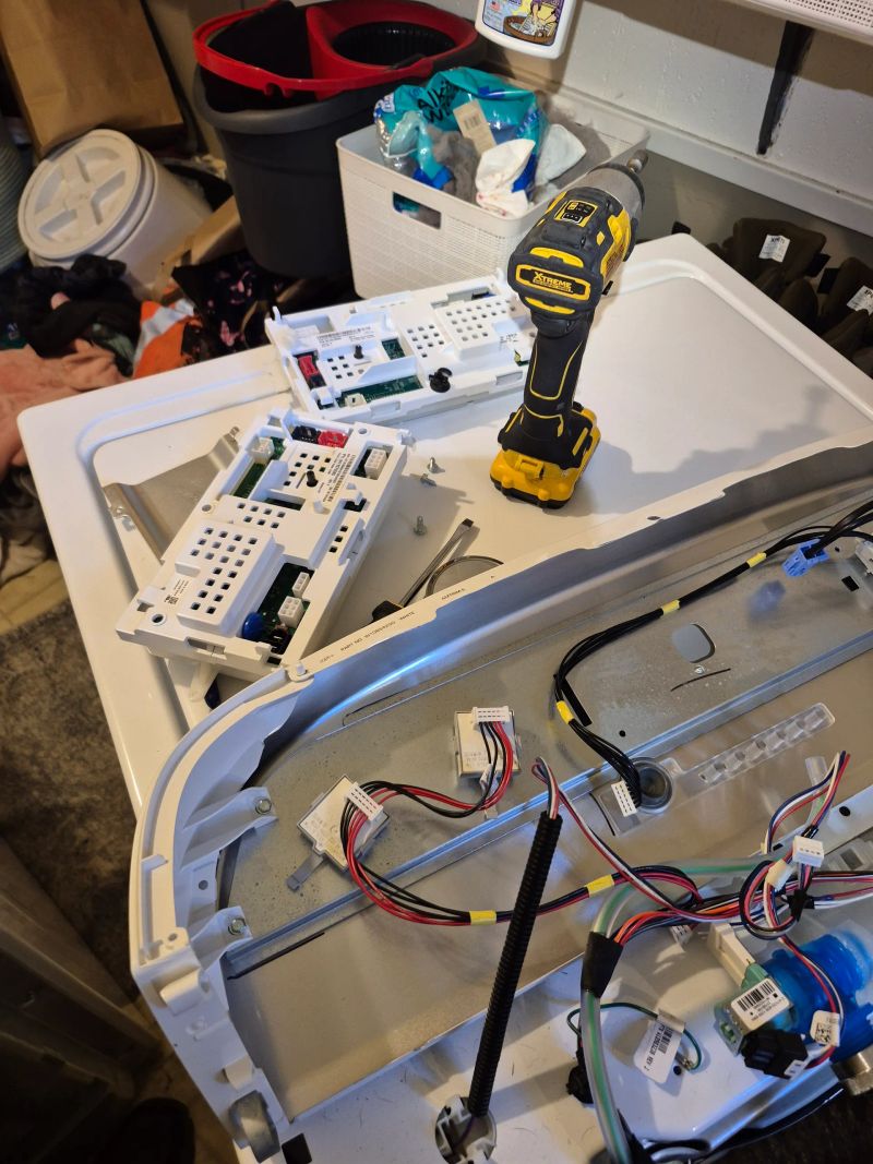 Disassembled electronic appliance with circuit boards, wires, and tools on a white work surface in a workshop or repair area.