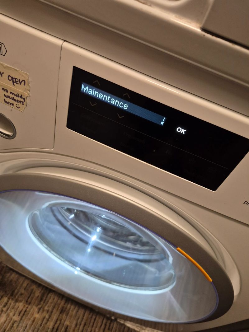 A washing machine screen displaying 'Maintenance' with an exclamation mark, indicating it needs service or repair.